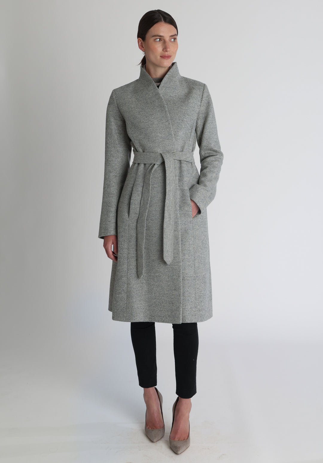 Model wearing the Hillsy coat in slate blue and cream lambswool twill, a wrap-style design with a standing collar and tie belt, offering a softly tailored, elegant silhouette. 