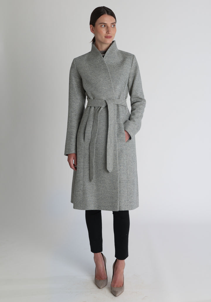Model wearing the Hillsy coat in slate blue and cream lambswool twill, a wrap-style design with a standing collar and tie belt, offering a softly tailored, elegant silhouette. 
