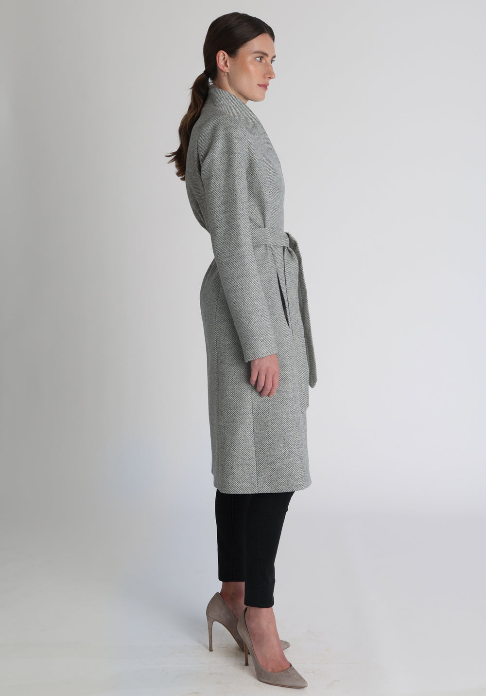 Model wearing the Hillsy coat in slate blue and cream lambswool twill, a wrap-style design with a standing collar and tie belt, offering a softly tailored, elegant silhouette. 