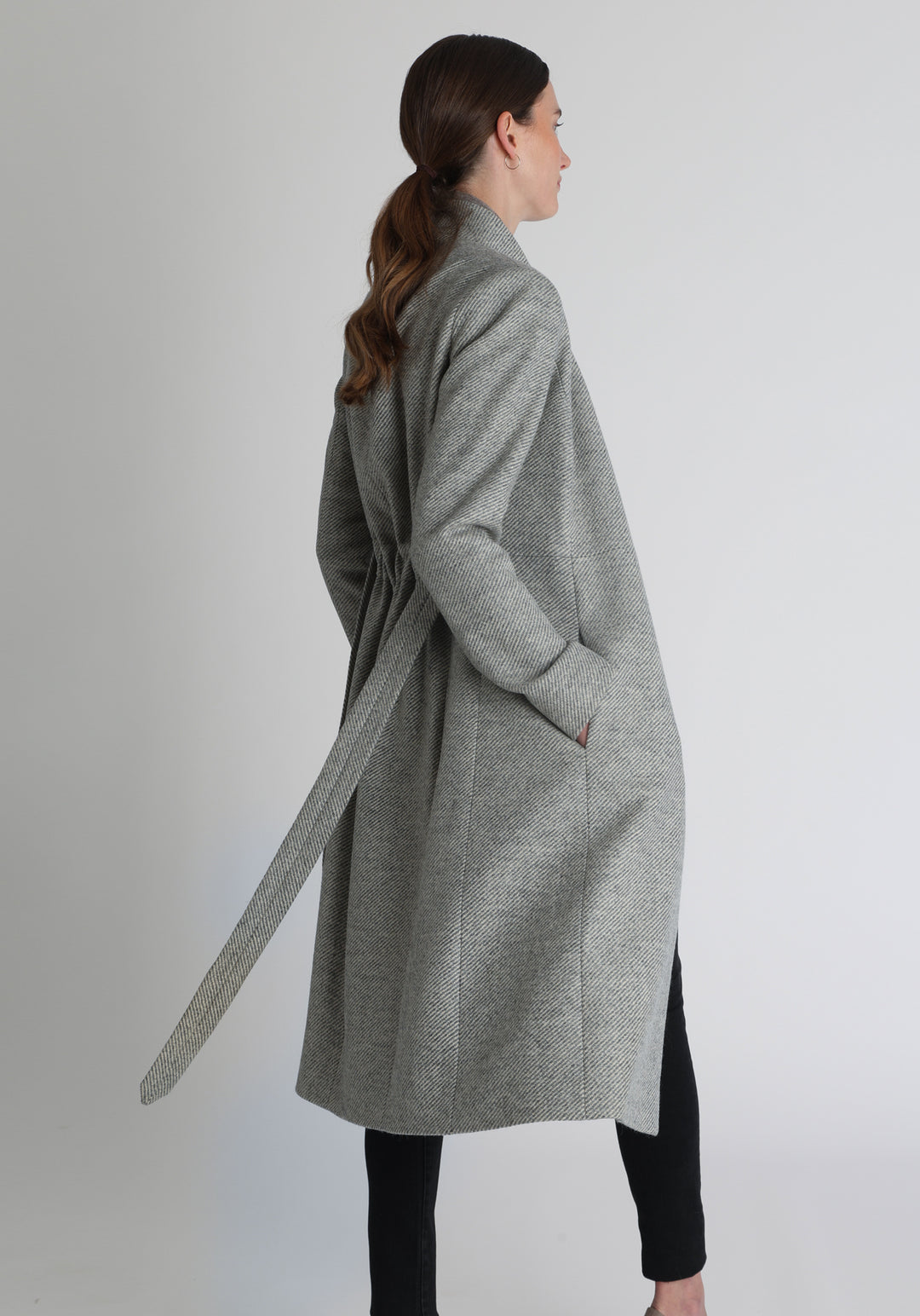 Model wearing the Hillsy coat in slate blue and cream lambswool twill, a wrap-style design with a standing collar and tie belt, offering a softly tailored, elegant silhouette. 