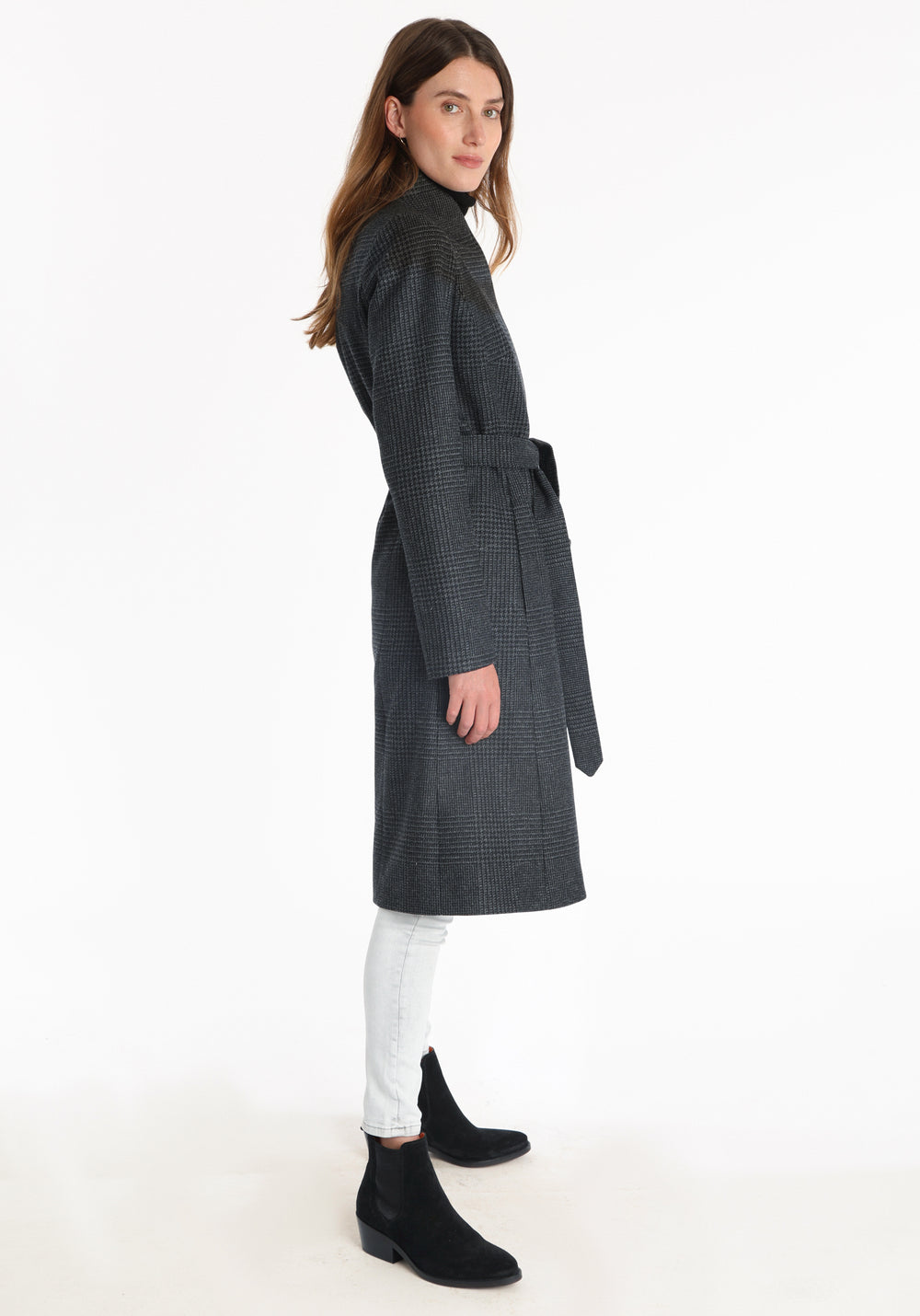 Model wearing the Hillsy coat in a black and charcoal grey Prince of Wales check, a wrap-style design with a standing collar, and tie belt, offering a softly tailored, elegant silhouette.