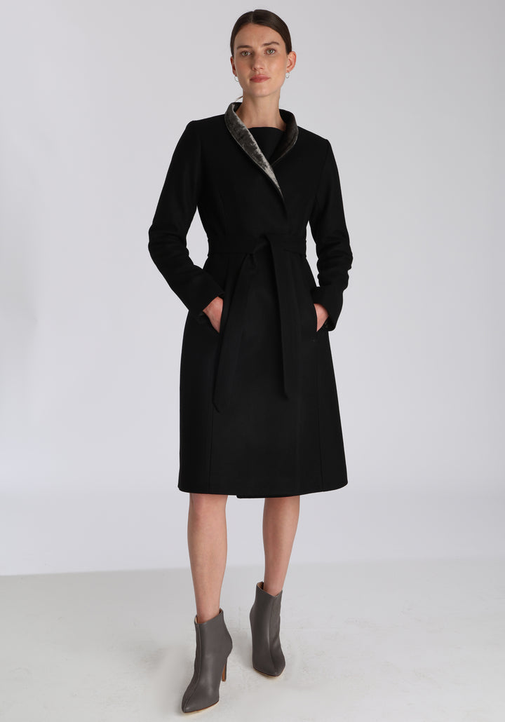 Model wearing the Hillsy coat in black wool cashmere felt, a wrap-style design with a standing collar, velvet trim, and tie belt, offering a softly tailored, elegant silhouette.