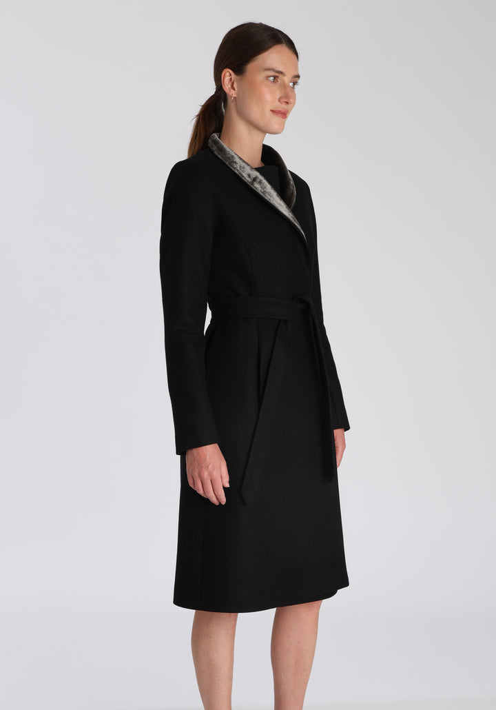 Model wearing the Hillsy coat in black wool cashmere felt, a wrap-style design with a standing collar, velvet trim, and tie belt, offering a softly tailored, elegant silhouette.