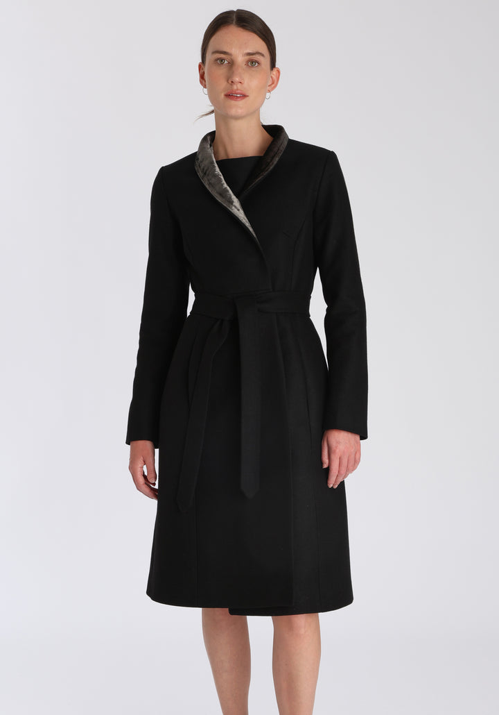 Model wearing the Hillsy coat in black wool cashmere felt, a wrap-style design with a standing collar, velvet trim, and tie belt, offering a softly tailored, elegant silhouette.