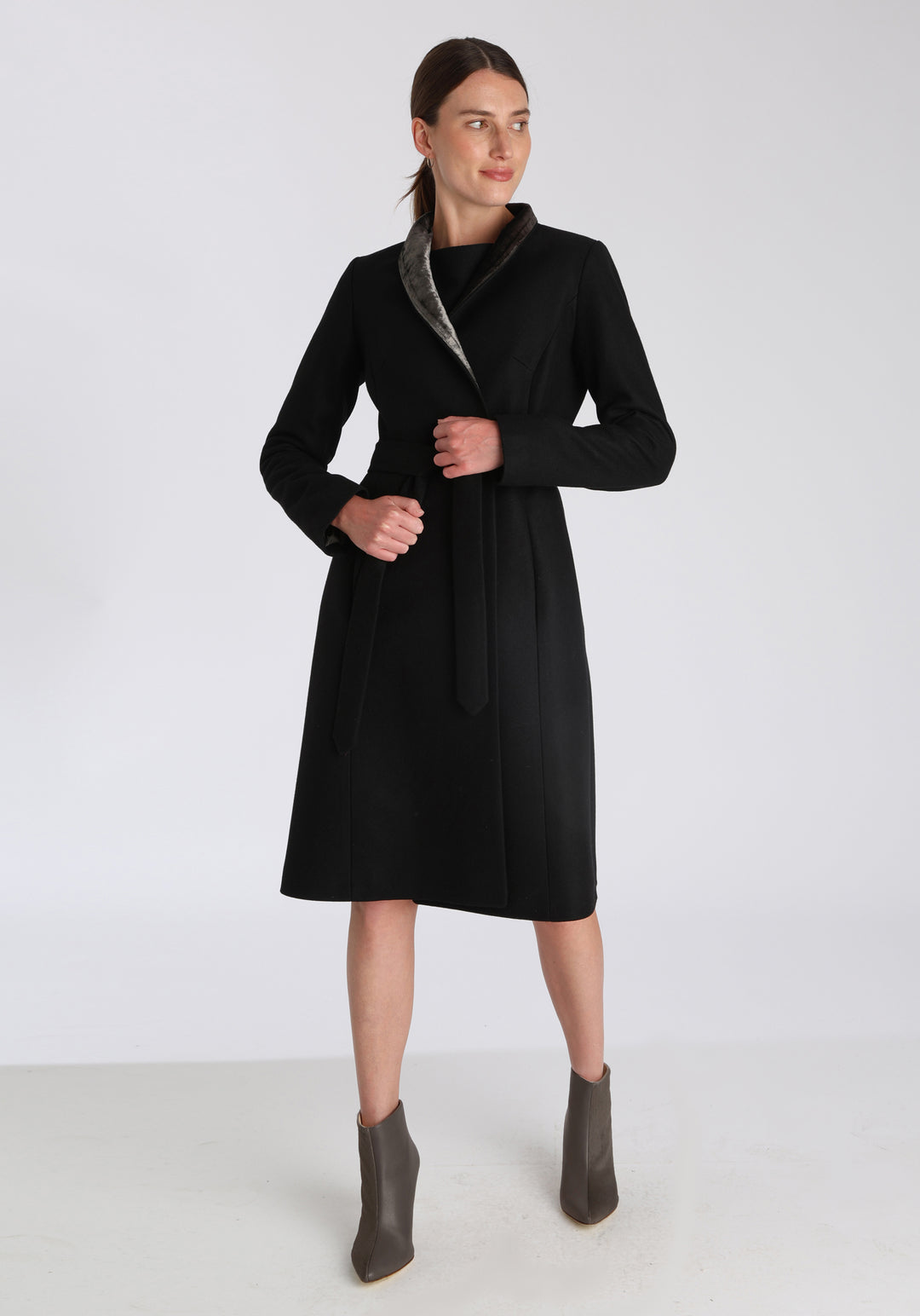 Model wearing the Hillsy coat in black wool cashmere felt, a wrap-style design with a standing collar, velvet trim, and tie belt, offering a softly tailored, elegant silhouette.