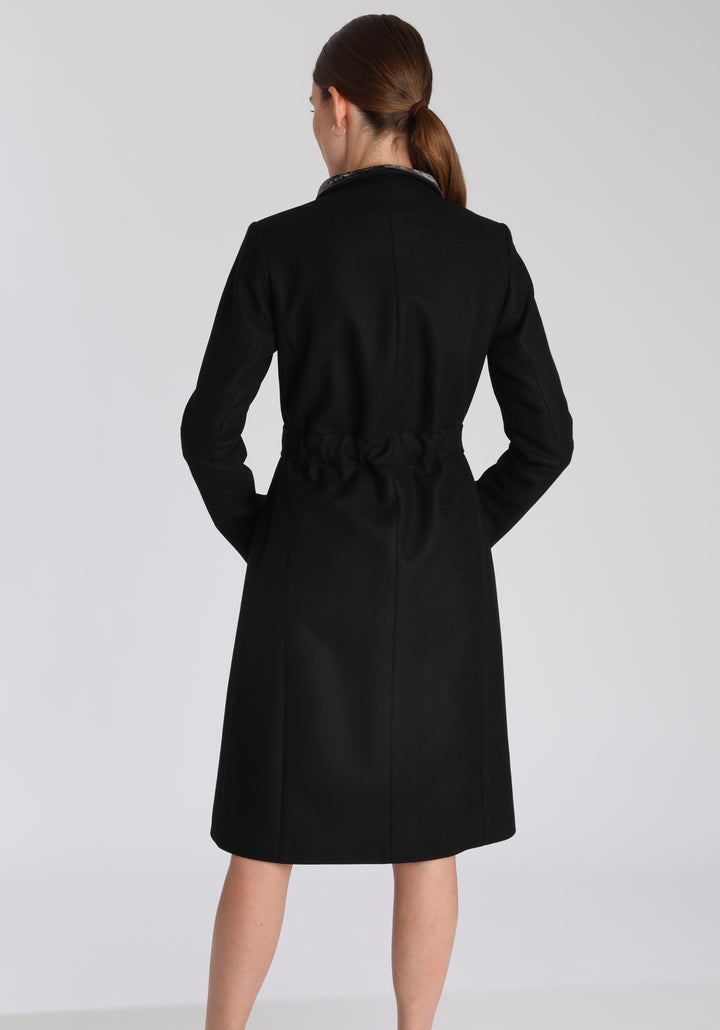 Model wearing the Hillsy coat in black wool cashmere felt, a wrap-style design with a standing collar, velvet trim, and tie belt, offering a softly tailored, elegant silhouette.