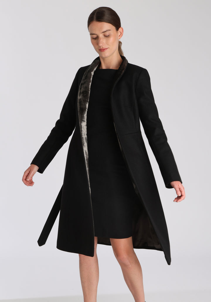 Model wearing the Hillsy coat in black wool cashmere felt, a wrap-style design with a standing collar, velvet trim, and tie belt, offering a softly tailored, elegant silhouette.