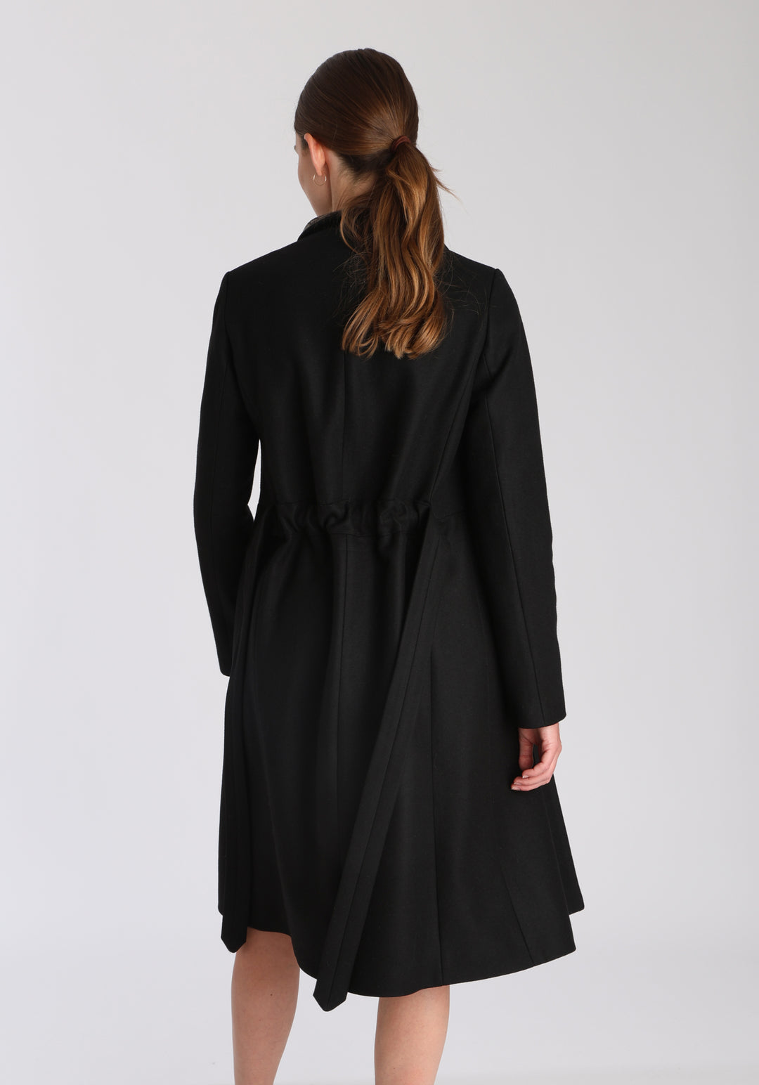 Model wearing the Hillsy coat in black wool cashmere felt, a wrap-style design with a standing collar, velvet trim, and tie belt, offering a softly tailored, elegant silhouette.