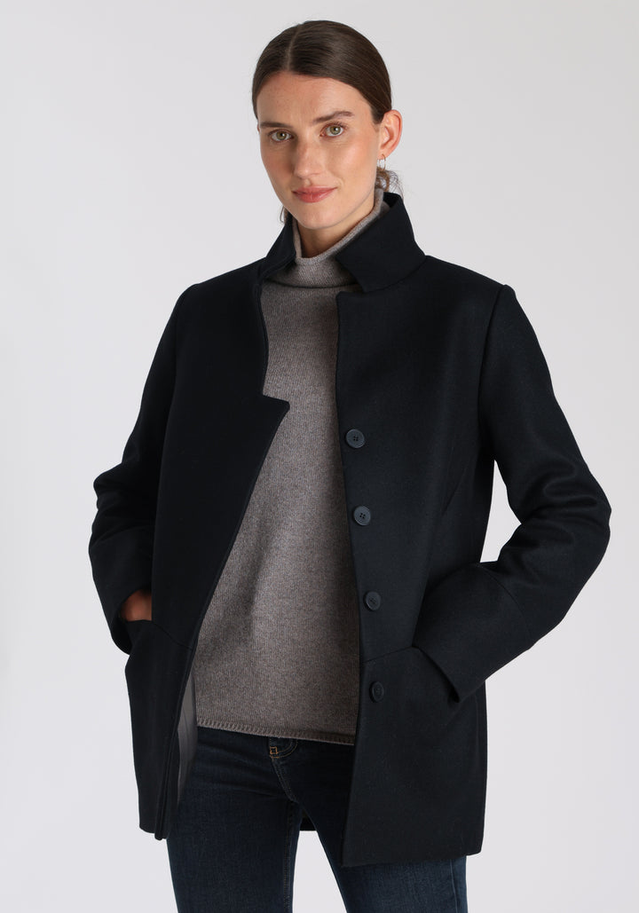 Model wearing the Jackson jacket in black cashmere blend, a structured, cocoon-shaped style with a cut-out standing collar, generous pockets, and deep panel detailing.