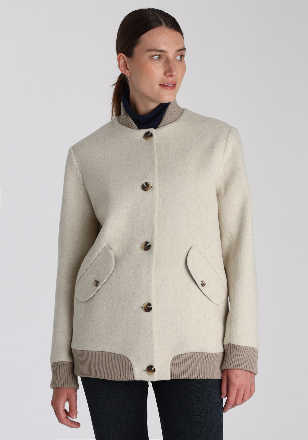 Model wearing the Jeffy jacket in cream merino wool, a baseball-inspired style with curved pocket flaps, front button fastenings, and ribbed knit trim, cut in a streamlined silhouette.