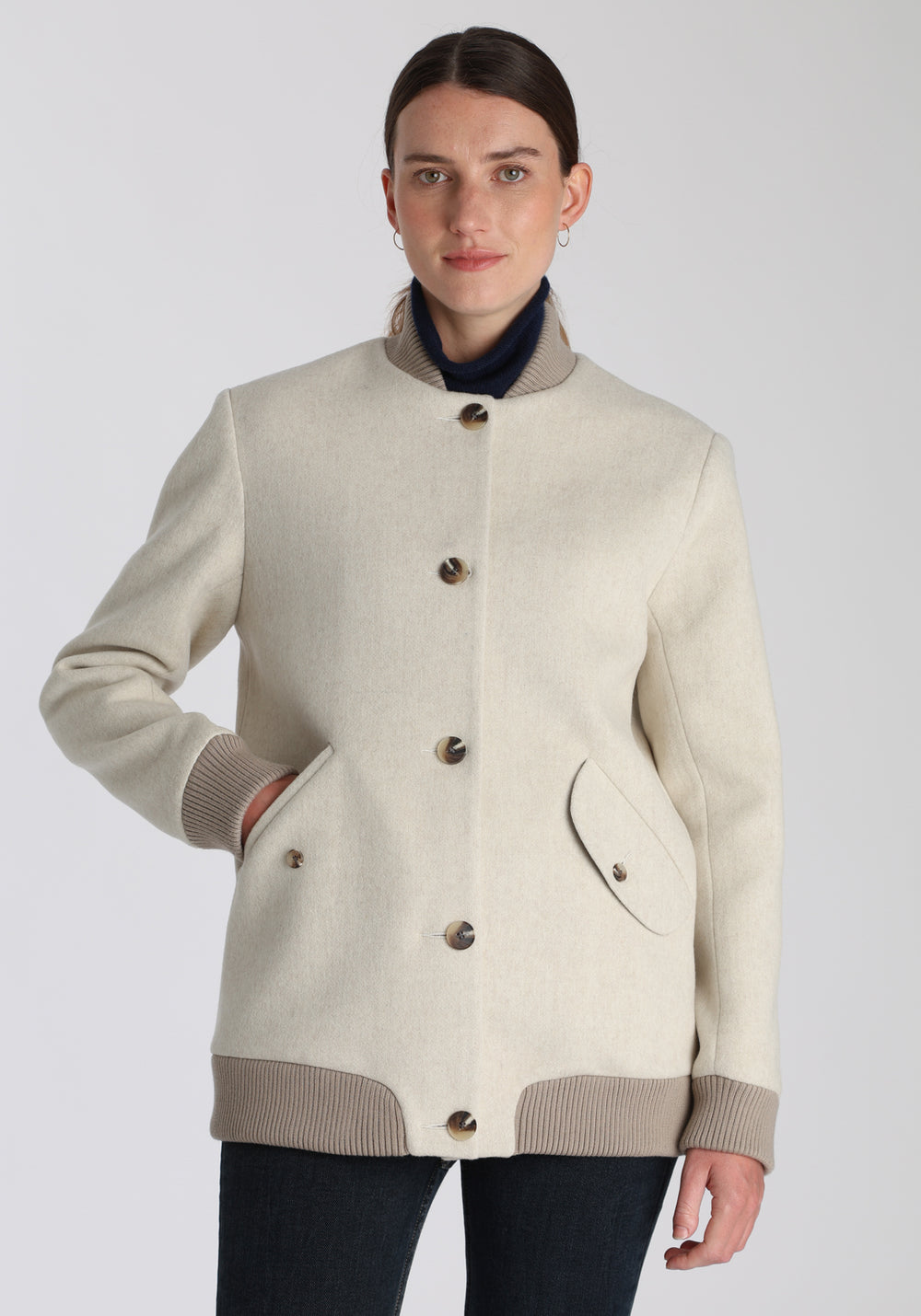 Model wearing the Jeffy jacket in cream merino wool, a baseball-inspired style with curved pocket flaps, front button fastenings, and ribbed knit trim, cut in a streamlined silhouette.
