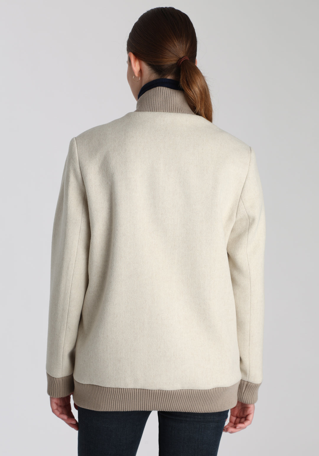 Model wearing the Jeffy jacket in cream merino wool, a baseball-inspired style with curved pocket flaps, front button fastenings, and ribbed knit trim, cut in a streamlined silhouette.
