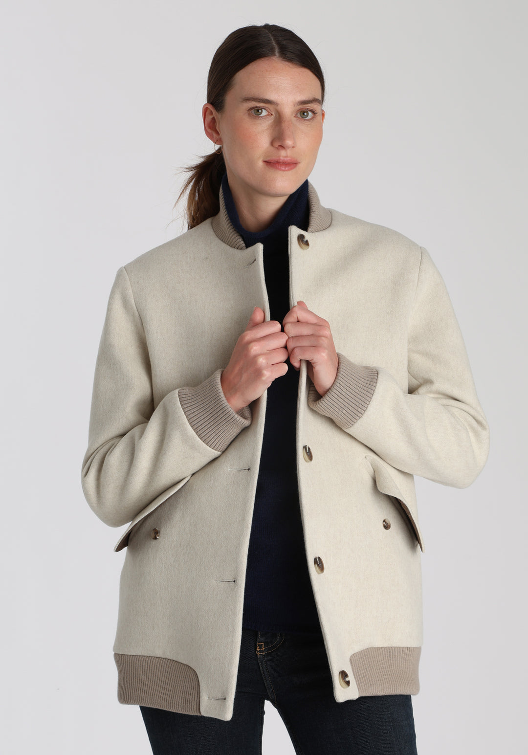 Model wearing the Jeffy jacket in cream merino wool, a baseball-inspired style with curved pocket flaps, front button fastenings, and ribbed knit trim, cut in a streamlined silhouette.