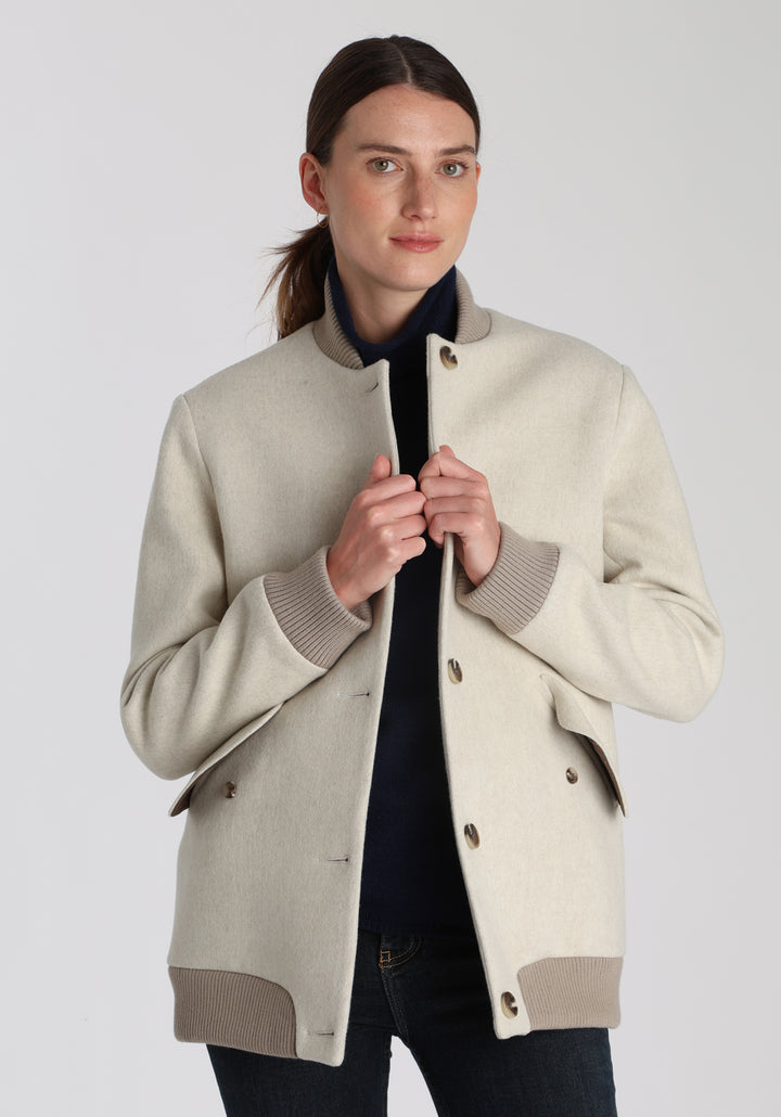 Model wearing the Jeffy jacket in cream merino wool, a baseball-inspired style with curved pocket flaps, front button fastenings, and ribbed knit trim, cut in a streamlined silhouette.