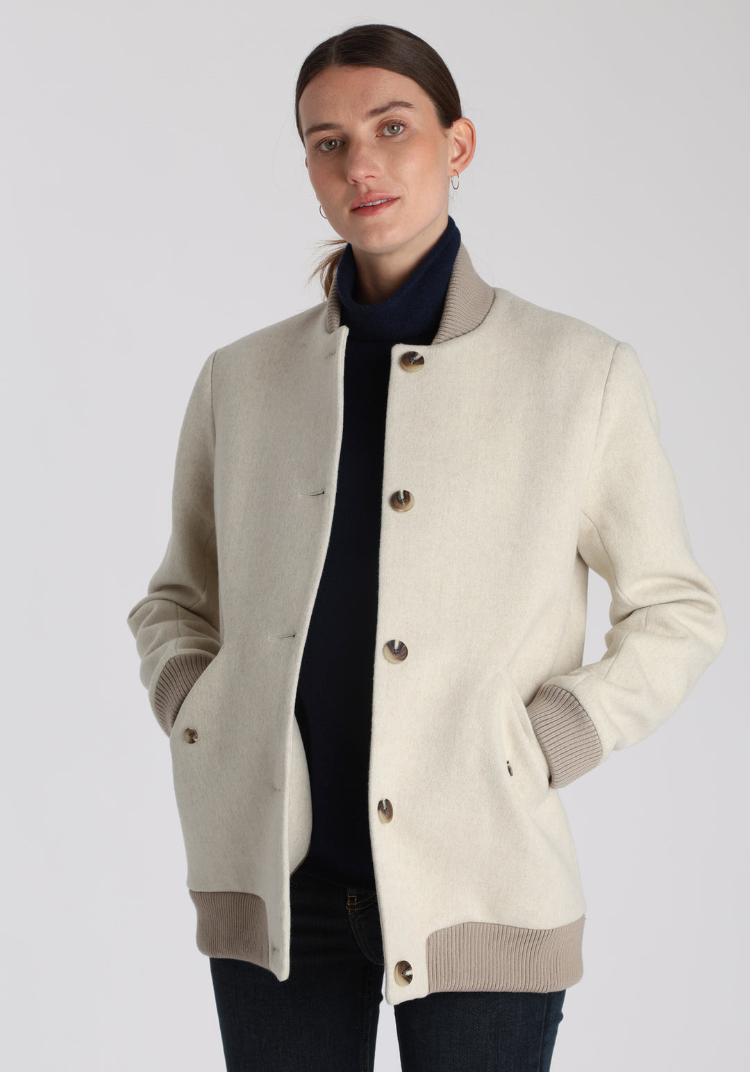 Model wearing the Jeffy jacket in cream merino wool, a baseball-inspired style with curved pocket flaps, front button fastenings, and ribbed knit trim, cut in a streamlined silhouette.