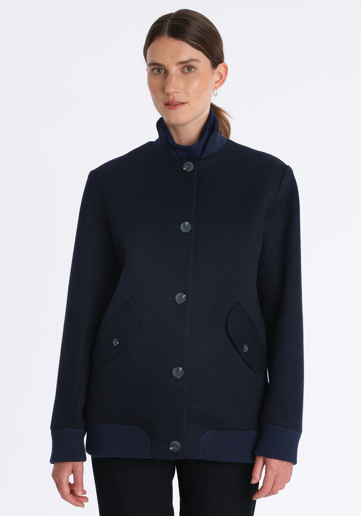 Model wearing the Jeffy jacket in navy merino wool, a baseball-inspired style with curved pocket flaps, front button fastenings, and ribbed knit trim, cut in a streamlined silhouette.