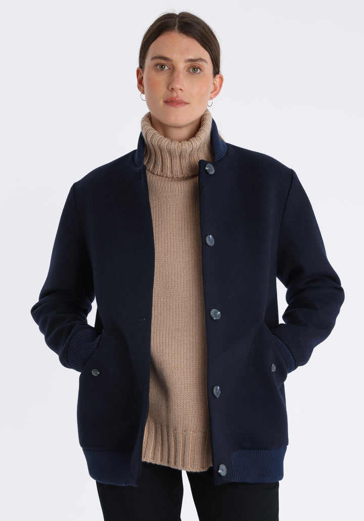 Model wearing the Jeffy jacket in navy merino wool, a baseball-inspired style with curved pocket flaps, front button fastenings, and ribbed knit trim, cut in a streamlined silhouette.