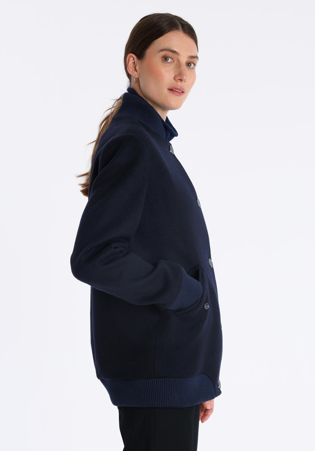 Model wearing the Jeffy jacket in navy merino wool, a baseball-inspired style with curved pocket flaps, front button fastenings, and ribbed knit trim, cut in a streamlined silhouette.