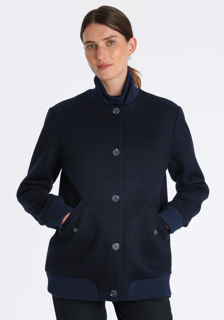 Model wearing the Jeffy jacket in navy merino wool, a baseball-inspired style with curved pocket flaps, front button fastenings, and ribbed knit trim, cut in a streamlined silhouette.