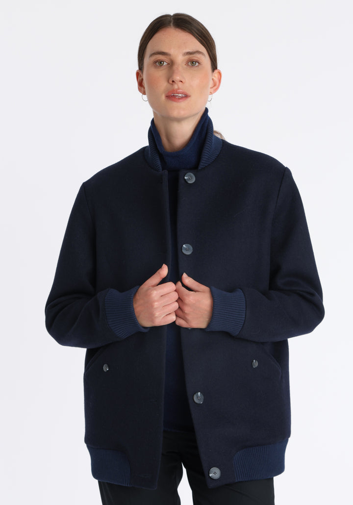 Model wearing the Jeffy jacket in navy merino wool, a baseball-inspired style with curved pocket flaps, front button fastenings, and ribbed knit trim, cut in a streamlined silhouette.