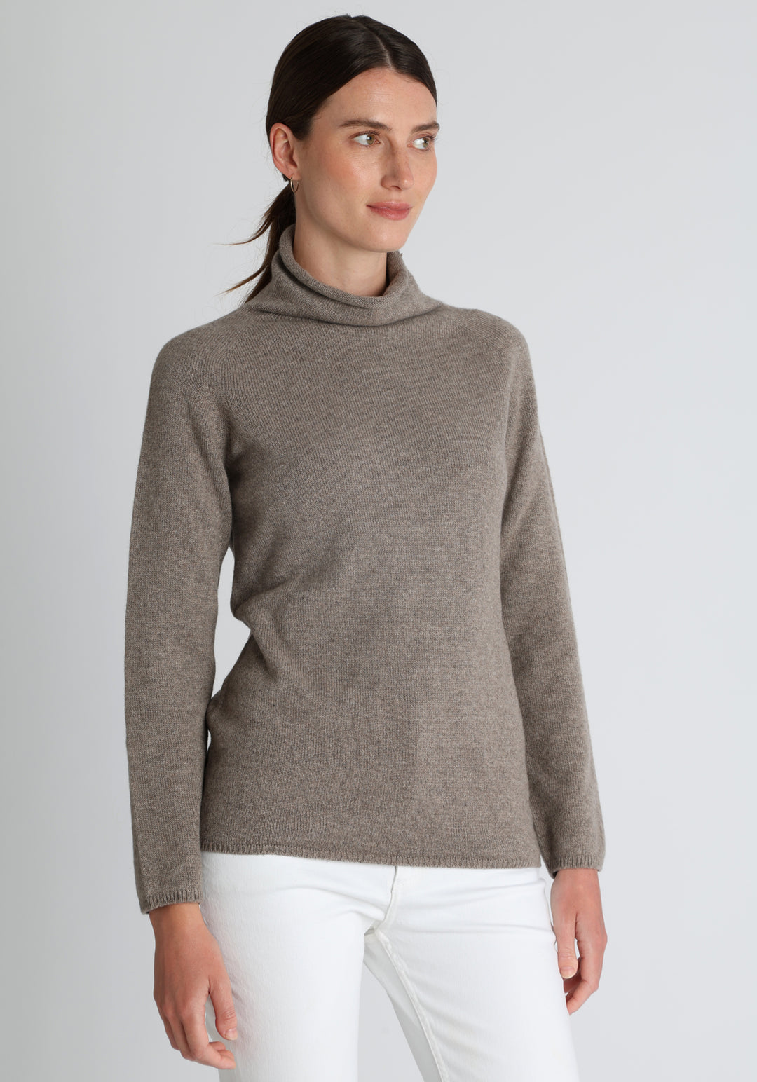 Model wearing the fine-knit cashmere jumper in mink, a slim fit style with a draped high neck, designed for layering and year-round wear.