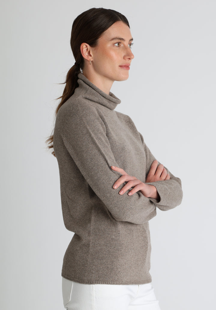 Model wearing the fine-knit cashmere jumper in mink, a slim fit style with a draped high neck, designed for layering and year-round wear.