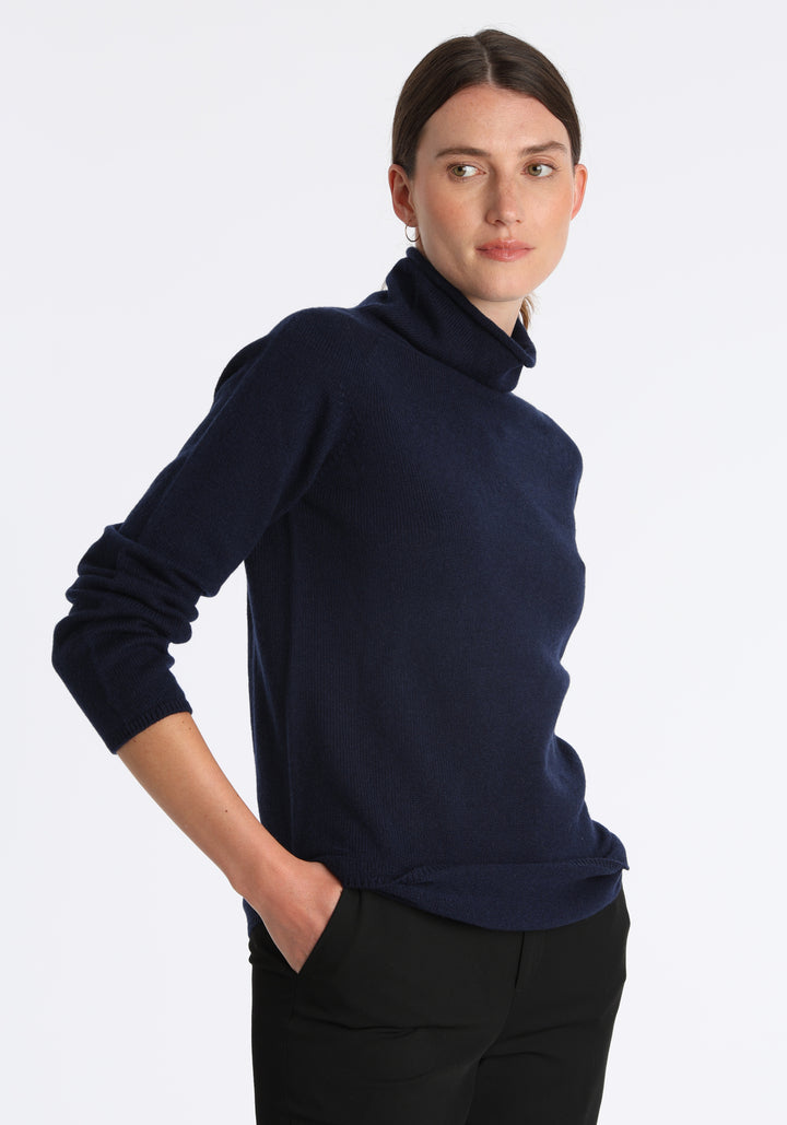 Model wearing the fine-knit cashmere jumper in navy, a slim fit style with a draped high neck, designed for layering and year-round wear.