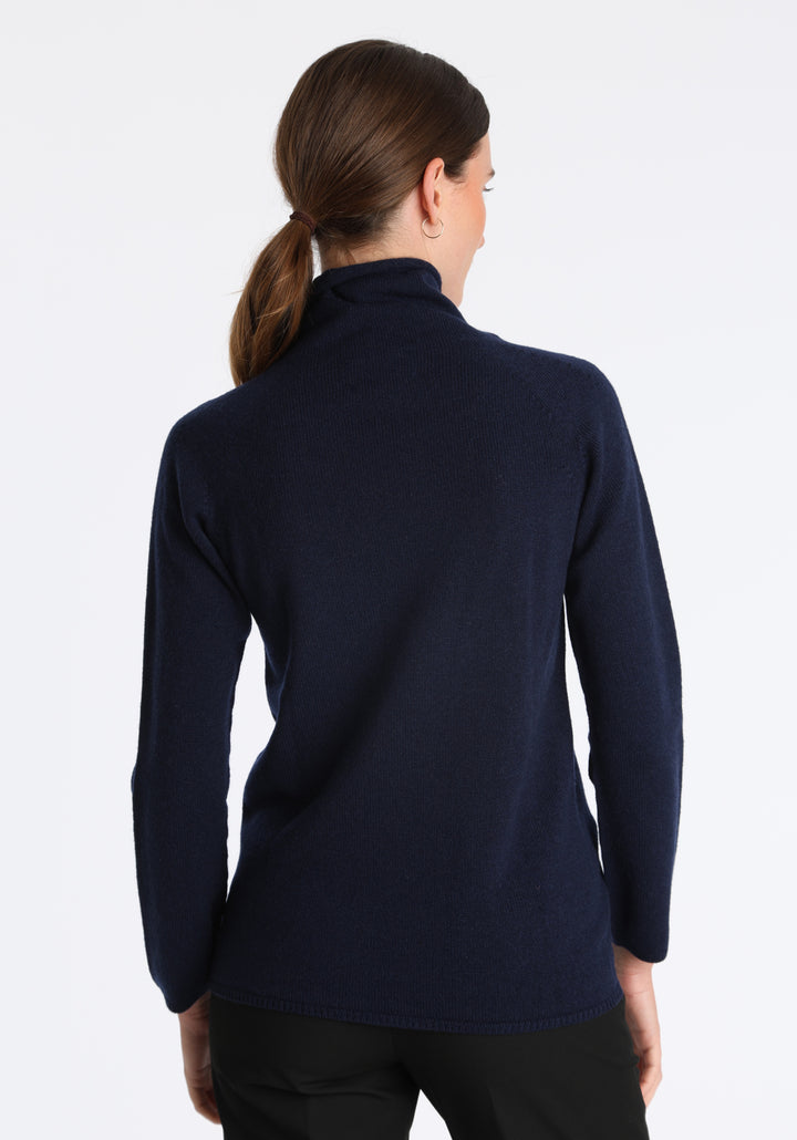 Model wearing the fine-knit cashmere jumper in navy, a slim fit style with a draped high neck, designed for layering and year-round wear.