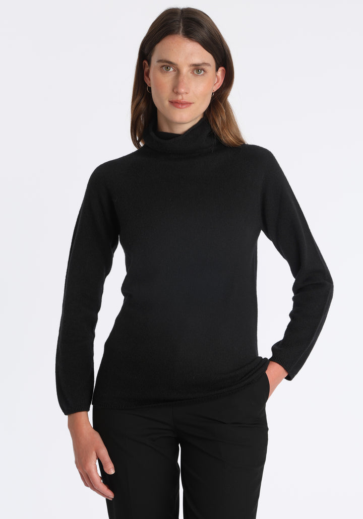 Model wearing the fine-knit cashmere jumper in black, a slim fit style with a draped high neck, designed for layering and year-round wear.