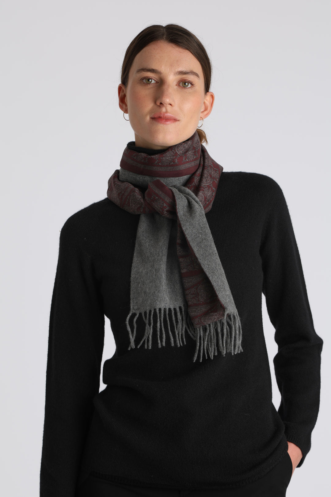Model wearing the grey cashmere scarf backed with burgundy paisley printed silk, over a black cashmere jumper.