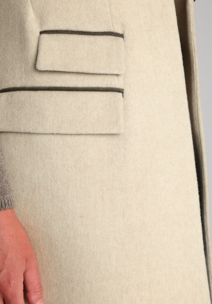 Model wearing the Kiekko waistcoat in cream merino wool with suede trim, a longline style featuring notched lapels, welt pockets, and a split back hem for ease of movement.