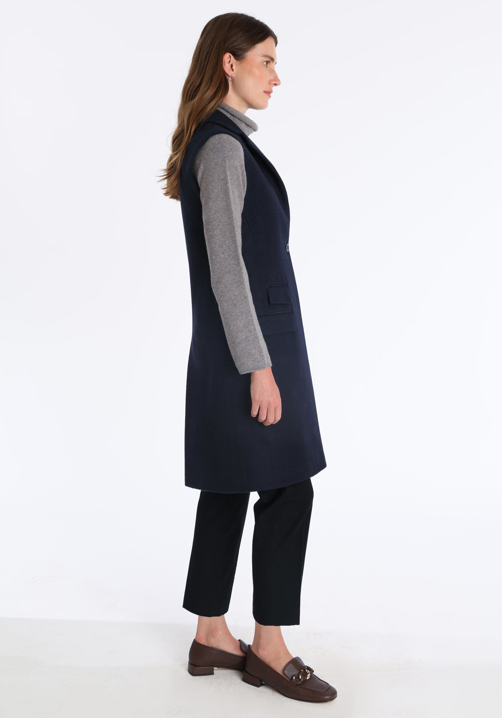 Model wearing the Kiekko waistcoat in navy merino wool with suede trim, a longline style featuring notched lapels, welt pockets, and a split back hem for ease of movement.
