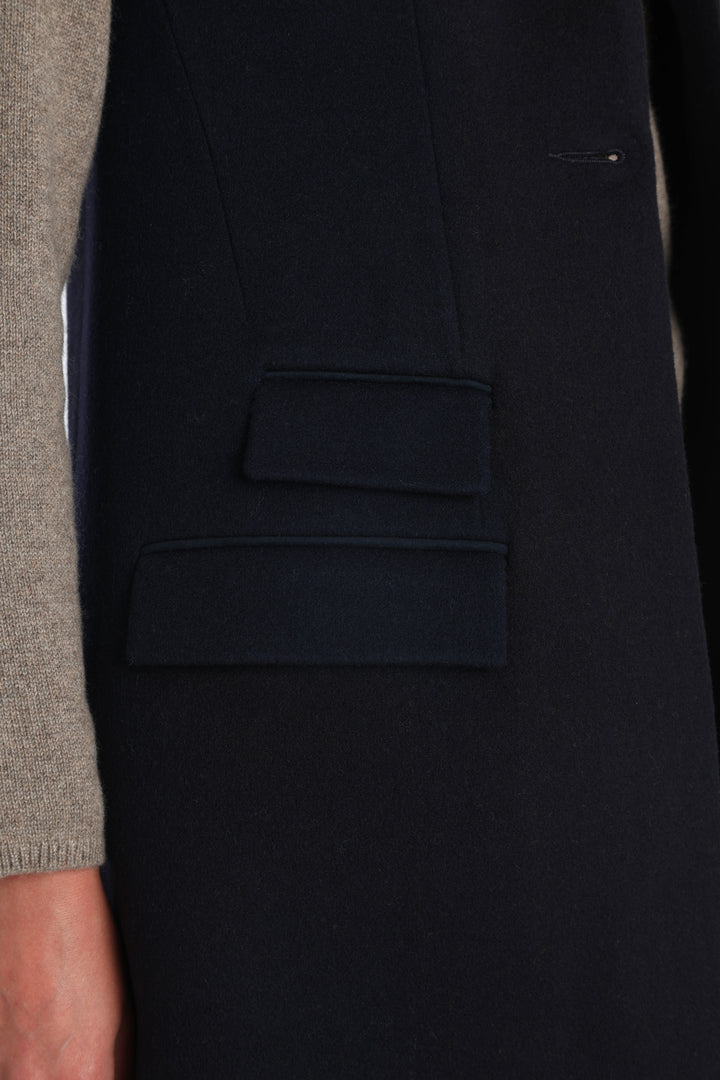Model wearing the Kiekko waistcoat in navy merino wool with suede trim, a longline style featuring notched lapels, welt pockets, and a split back hem for ease of movement.