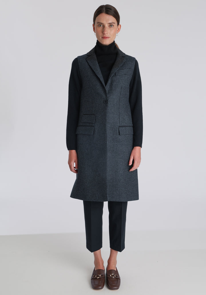 Model wearing the Kiekko waistcoat in black and grey Prince of Wales check with suede trim, a long line style featuring notched lapels, welt pockets, and a split back hem for ease of movement.