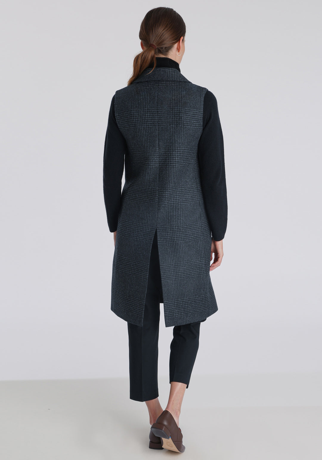Model wearing the Kiekko waistcoat in black and grey Prince of Wales check with suede trim, a long line style featuring notched lapels, welt pockets, and a split back hem for ease of movement.