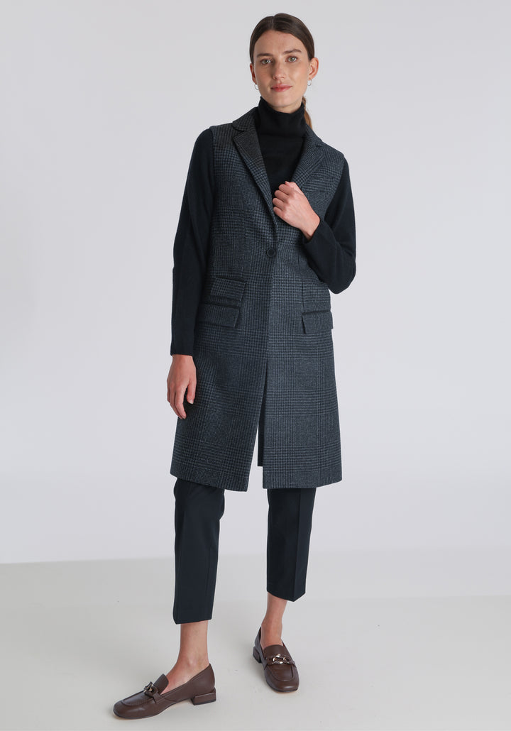 Model wearing the Kiekko waistcoat in black and grey Prince of Wales check with suede trim, a long line style featuring notched lapels, welt pockets, and a split back hem for ease of movement.