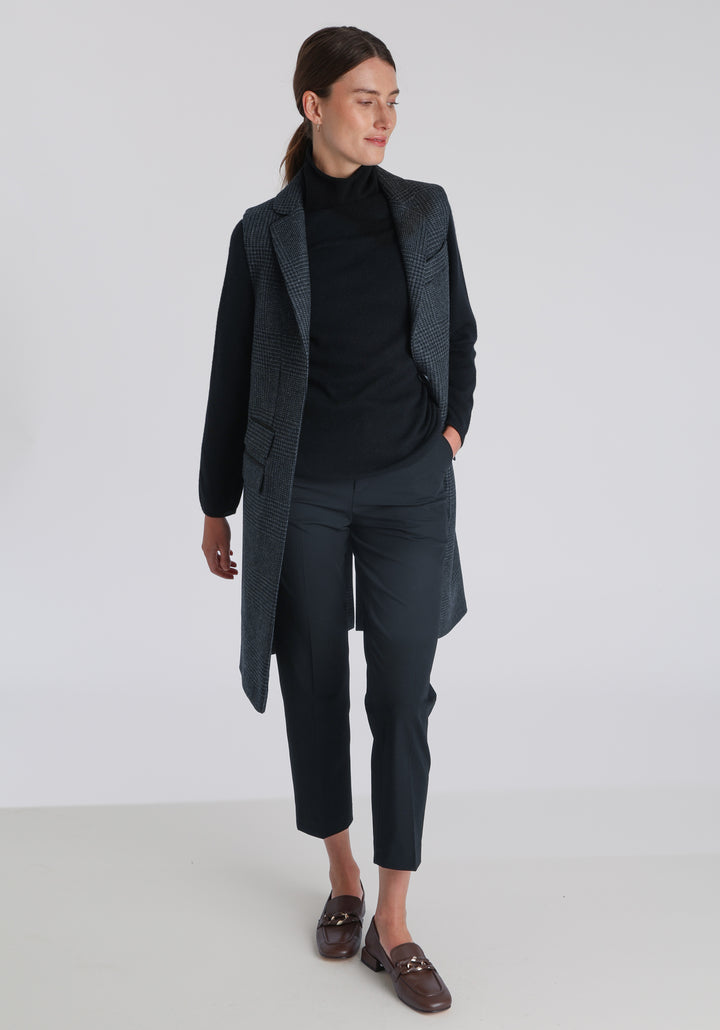 Model wearing the Kiekko waistcoat in black and grey Prince of Wales check with suede trim, a long line style featuring notched lapels, welt pockets, and a split back hem for ease of movement.