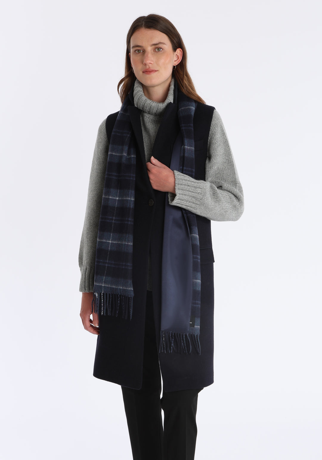Model wearing the midnight check cashmere scarf backed with navy silk, over the Kiekko waistcoat in navy and a chunky roll neck grey marl jumper.