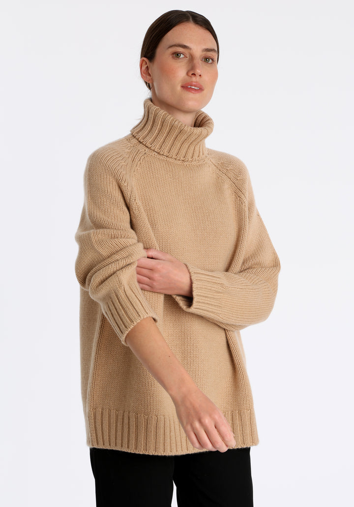 Model wearing the chunky roll neck jumper in dune Scottish cashmere—a one-size knit with dropped shoulders, ribbed trims, and a softly structured silhouette