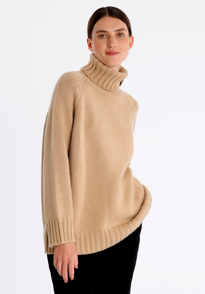 Model wearing the chunky roll neck jumper in dune Scottish cashmere—a one-size knit with dropped shoulders, ribbed trims, and a softly structured silhouette