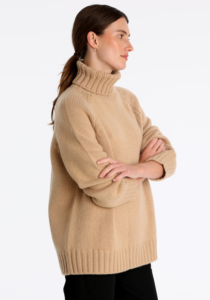 Model wearing the chunky roll neck jumper in dune Scottish cashmere—a one-size knit with dropped shoulders, ribbed trims, and a softly structured silhouette