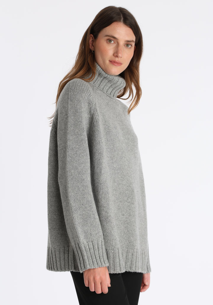 Model wearing the chunky roll neck jumper in grey marl Scottish cashmere—a one-size knit with dropped shoulders, ribbed trims, and a softly structured silhouette.