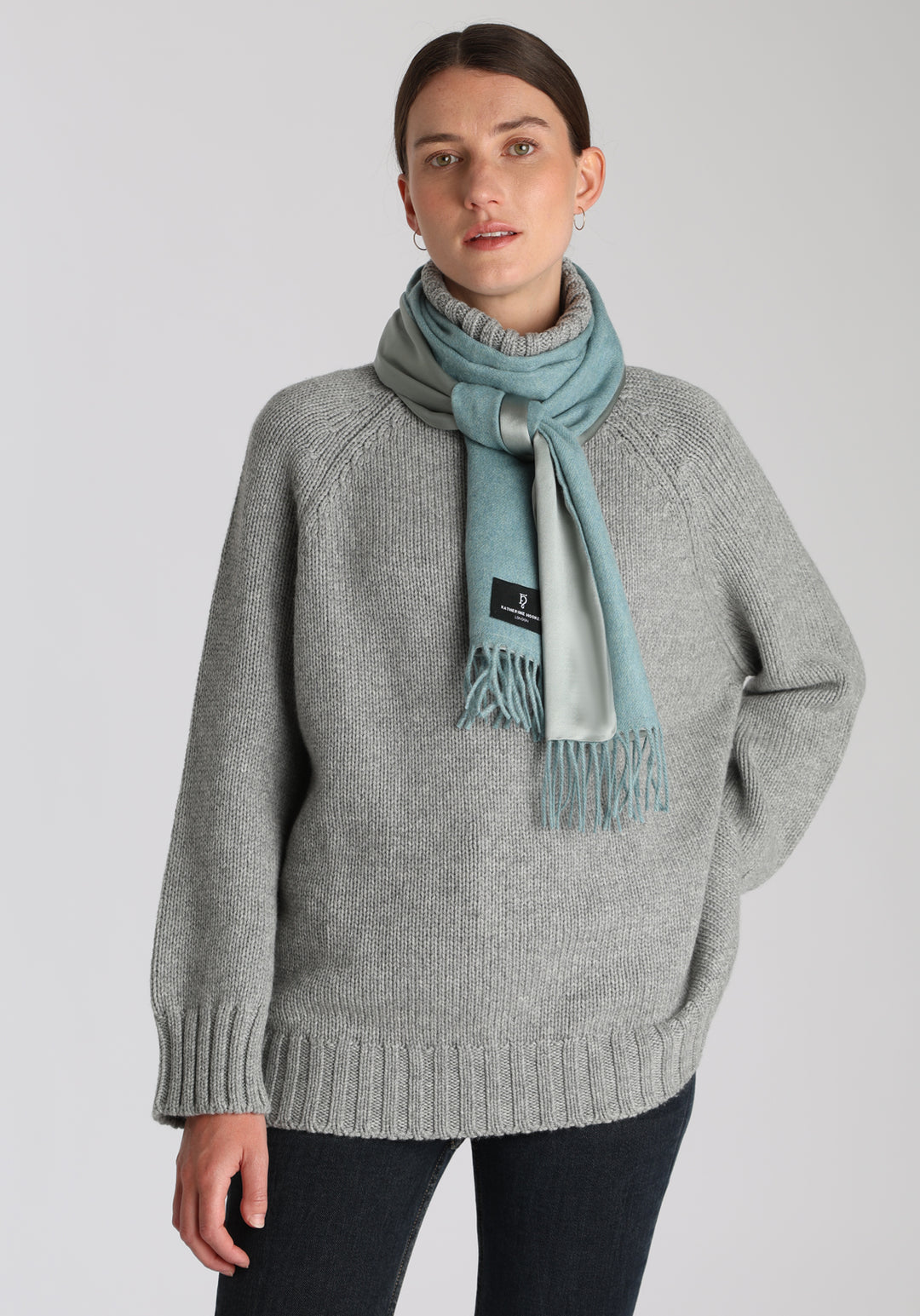 Model wearing the sky blue cashmere scarf backed with silver blue silk, over a chunky roll neck jumper in grey marl.