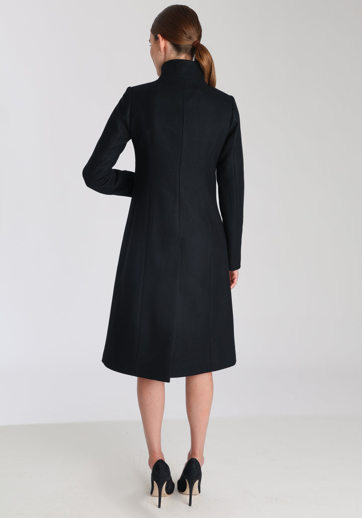 Model wearing the Opera coat in black cashmere blend, an elegant, knee-length style with a high funnel neck, curved front pockets, and a slim, waist-contouring silhouette.