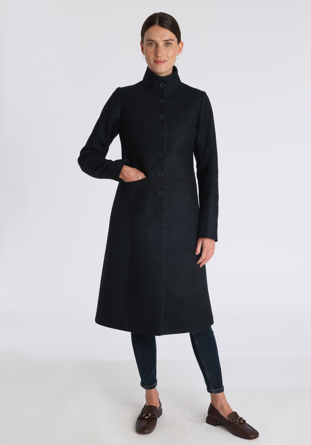 Model wearing the Opera coat in black cashmere blend, an elegant, knee-length style with a high funnel neck, curved front pockets, and a slim, waist-contouring silhouette.