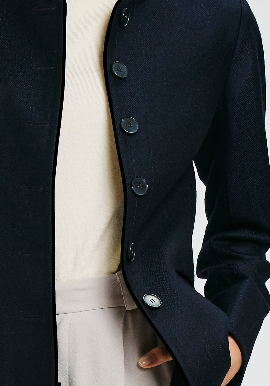Model wearing the Patmos jacket in navy herringbone lambswool with short pile black cotton velvet trim, a slim-fit style featuring a mandarin collar, front pockets, and generous sleeves with slate button detailing.