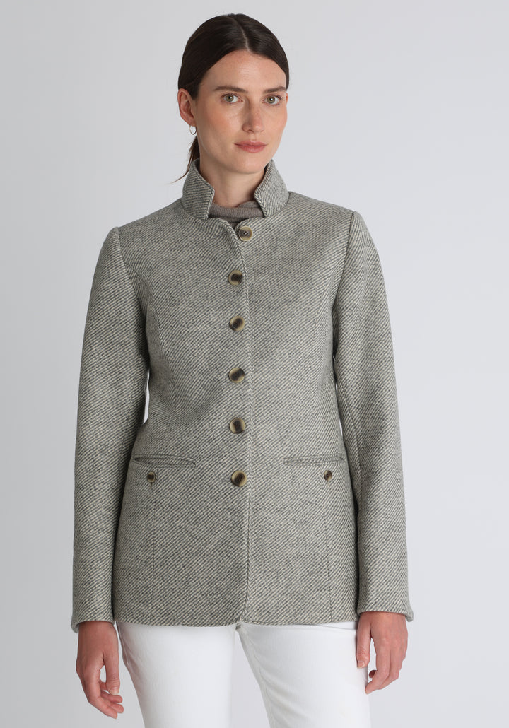 Model wearing the Patmos jacket in slate blue and cream lambswool wool with suede trim, a slim-fit style featuring a mandarin collar, front pockets, and generous sleeves with button detailing.