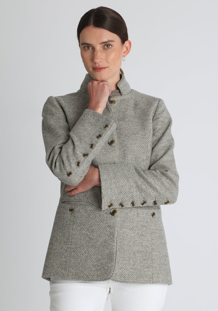 Model wearing the Patmos jacket in slate blue and cream lambswool wool with suede trim, a slim-fit style featuring a mandarin collar, front pockets, and generous sleeves with button detailing.