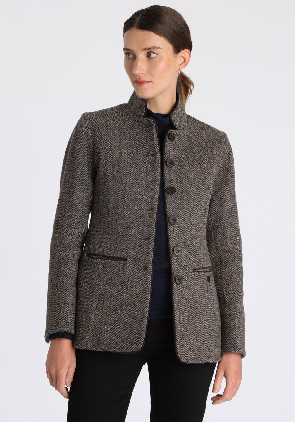 Model wearing the Patmos jacket in heather herringbone Harris Tweed with suede trim, a slim-fit style featuring a mandarin collar, front pockets, and generous sleeves with button detailing.