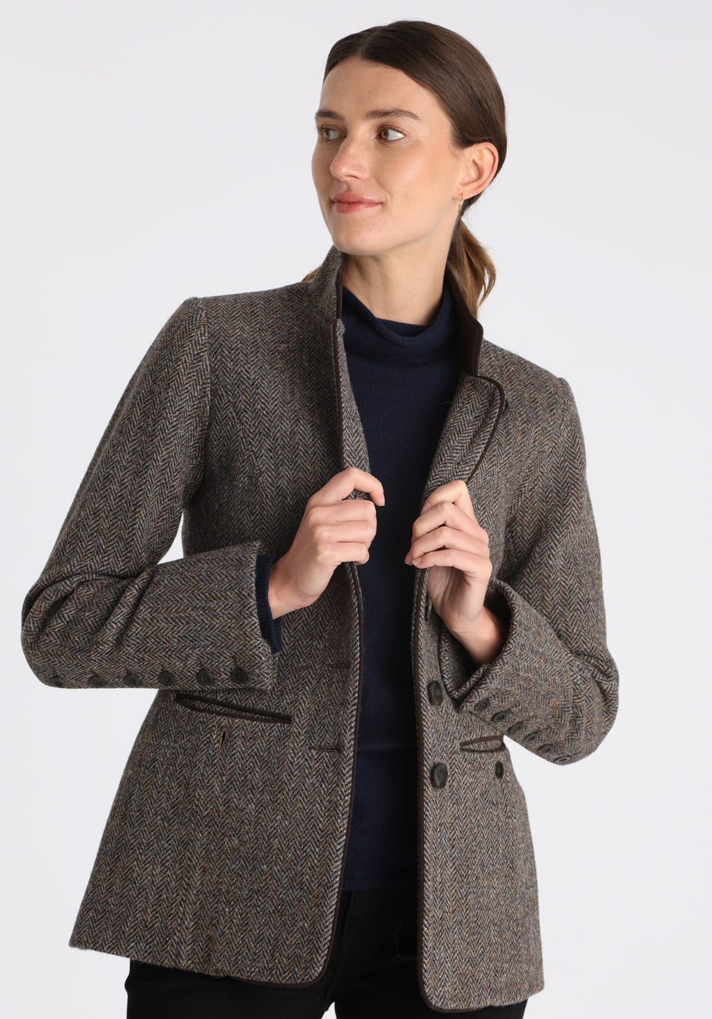 Model wearing the Patmos jacket in heather herringbone Harris Tweed with suede trim, a slim-fit style featuring a mandarin collar, front pockets, and generous sleeves with button detailing.
